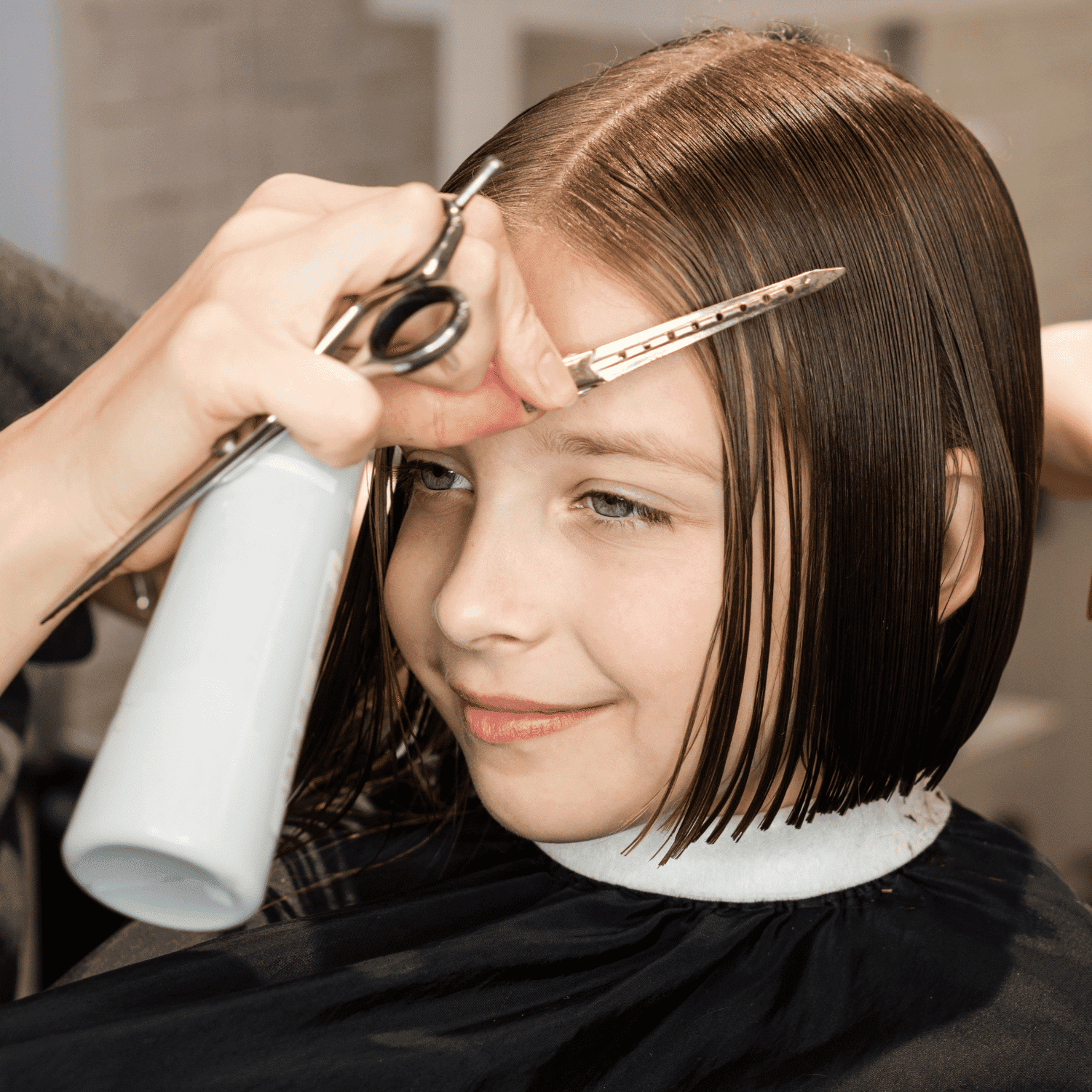 Young girl receiving a haircut, stylist using scissors on her wet, chin-length hair.