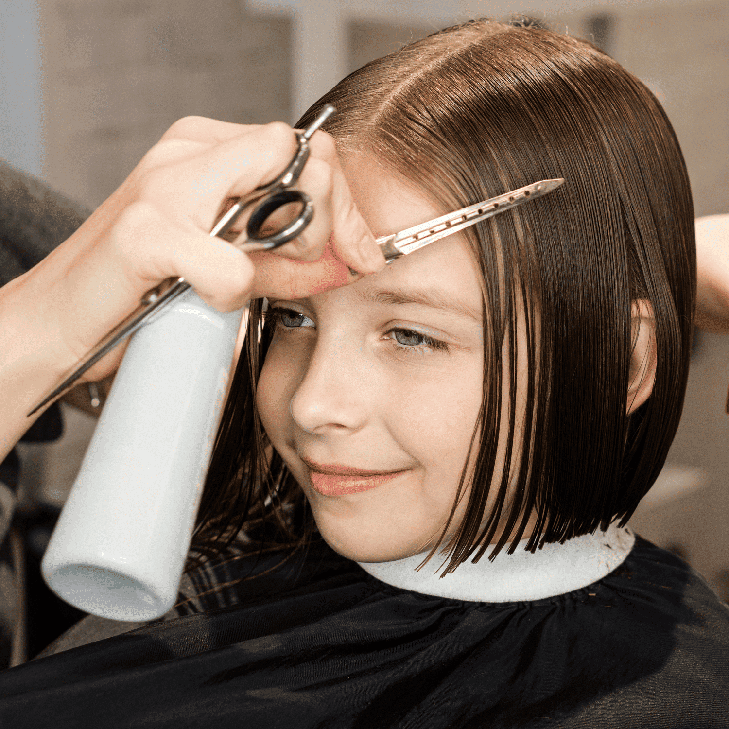 Young girl receiving a haircut, stylist using scissors on her wet, chin-length hair.