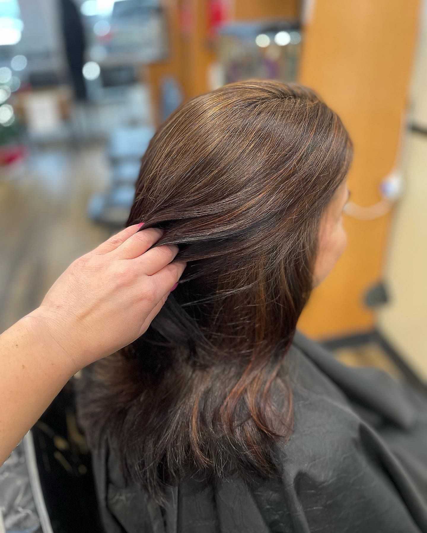 Hand showing off shiny, freshly highlighted brown hair in a salon setting.
