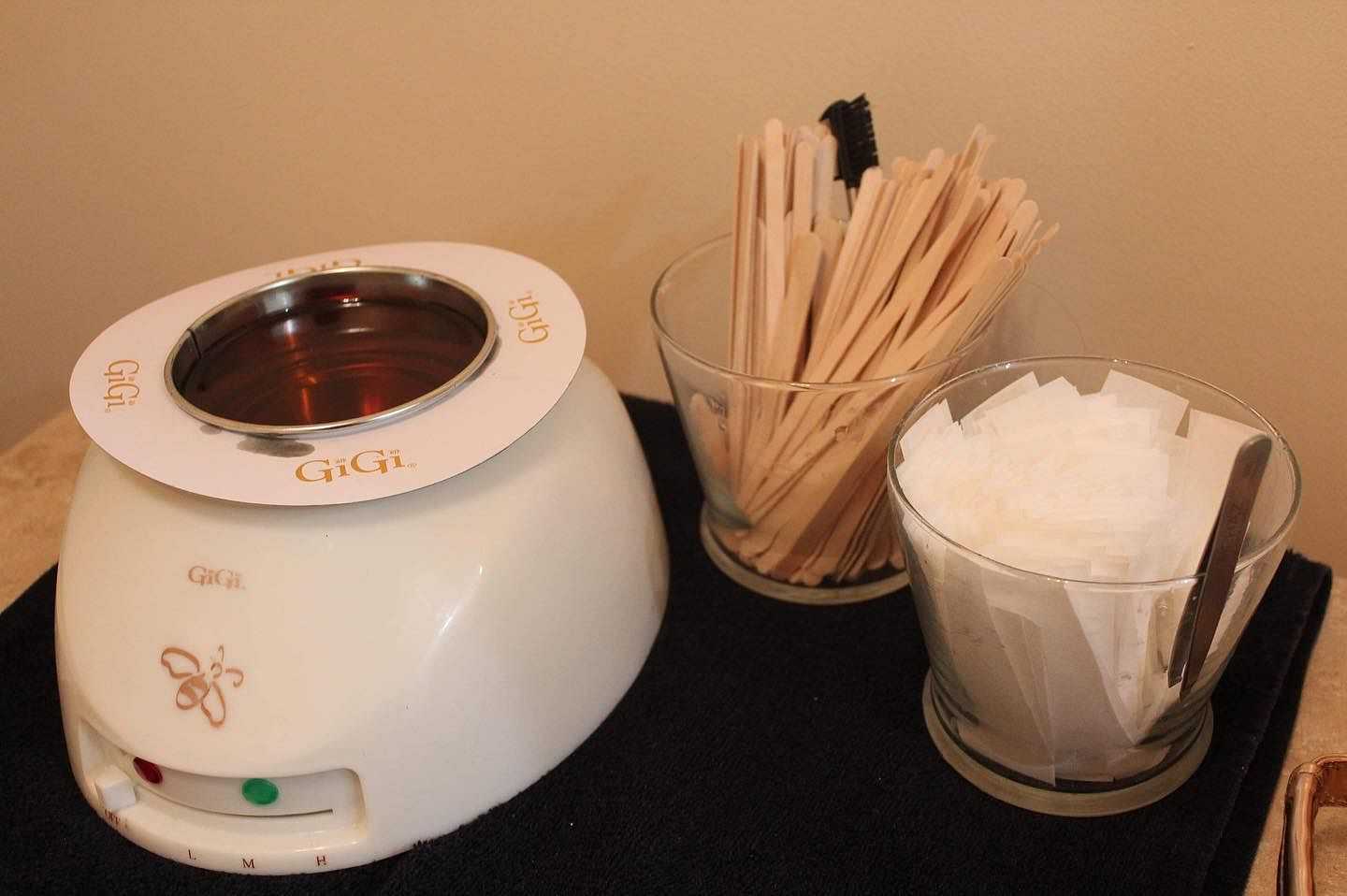 Wax warmer with GiGi branding, wooden spatulas, and cloth strips on a black mat.