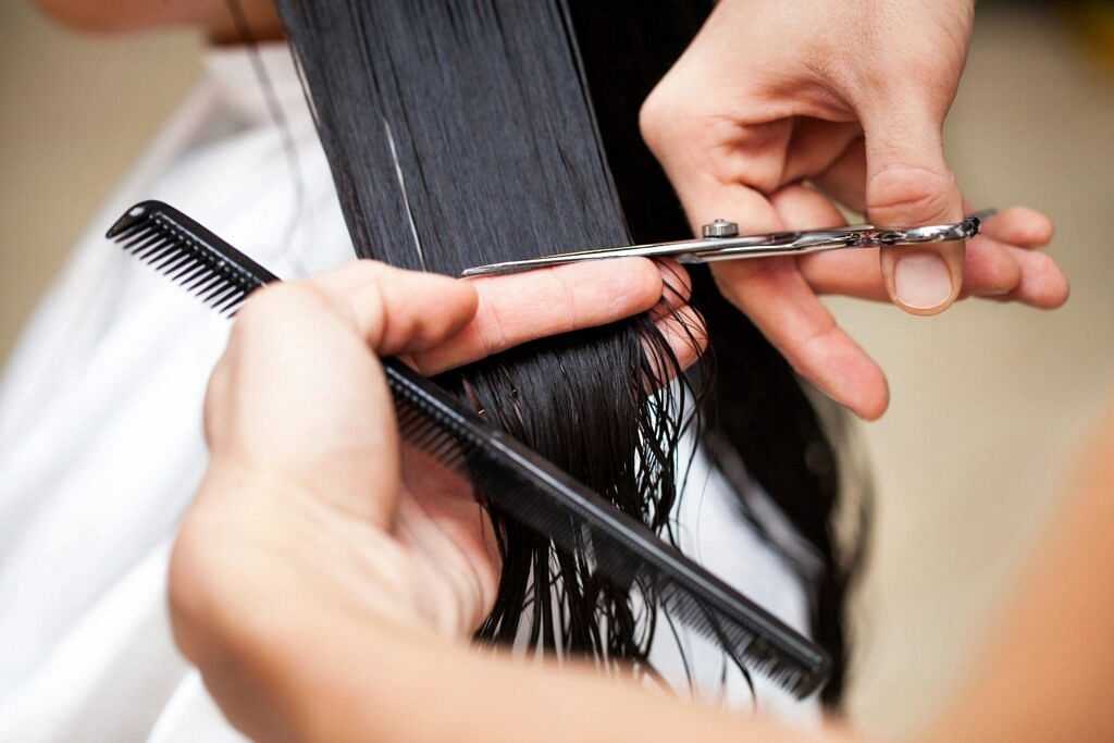 Hairdresser cutting long black hair with scissors while holding a comb for precision.