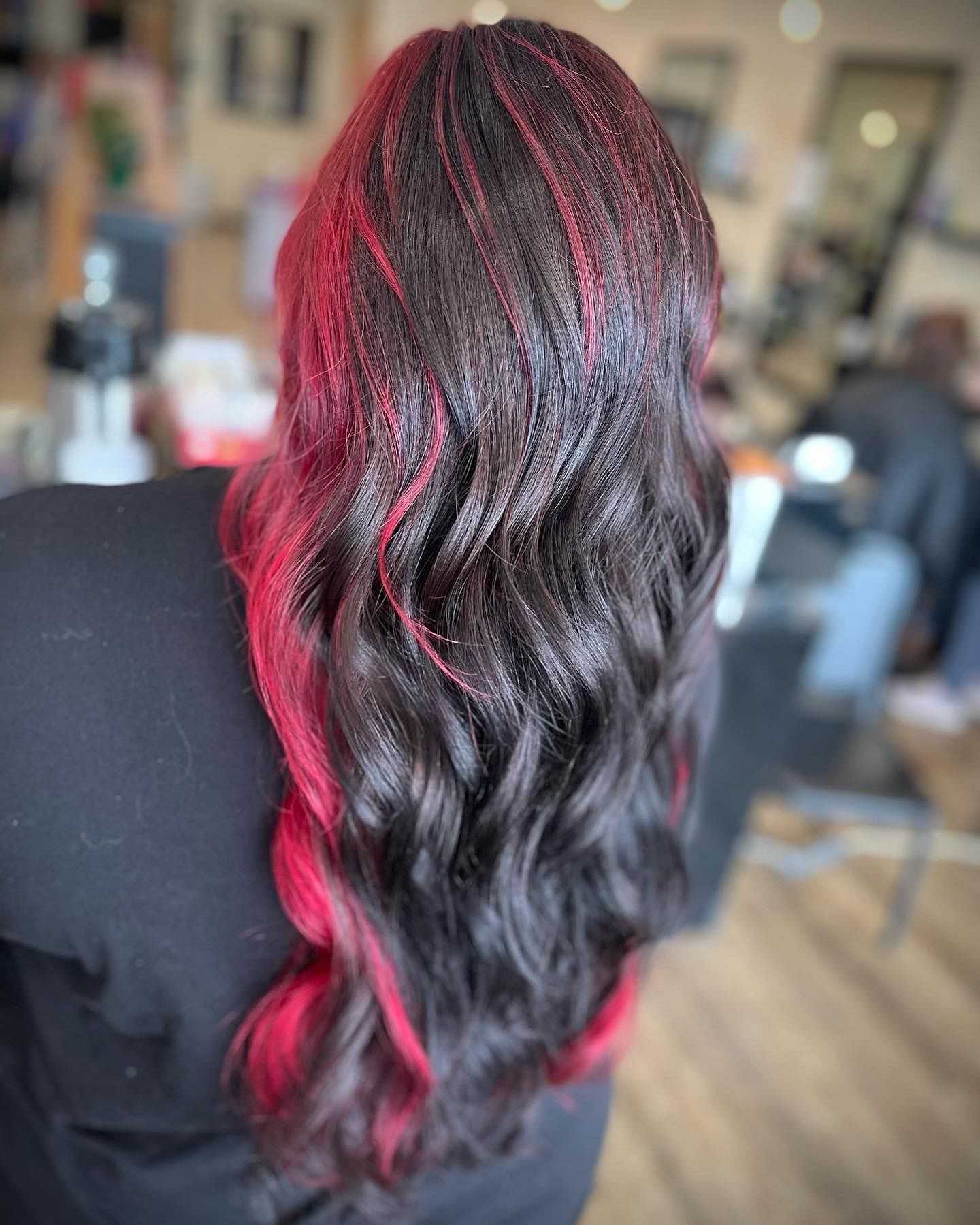 Woman with long, wavy brown hair featuring vibrant red highlights in a salon setting.