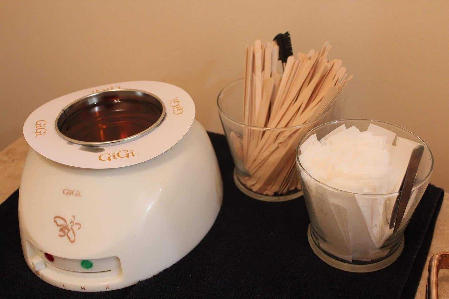 Wax warmer with GiGi branding, wooden spatulas, and cloth strips on a black mat.